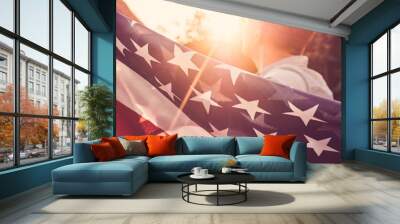 Handsome man waving an American flag against a background of trees and blue sky. View from the back, close-up. National holiday concept Wall mural