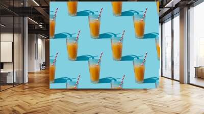 Seamless pattern of a glass with orange juice and a straw on a blue background Wall mural