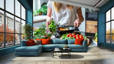 Young woman is cooking healthy food in her kitchen. Fresh vegetables in pan Wall mural