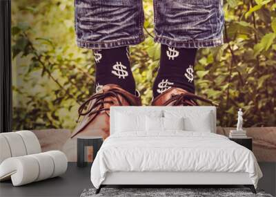 Men's legs in stylish shoes, black socks with patterns in the form of US dollars on a wooden terrace against the background of green trees. Beauty, fashion, elegance Wall mural