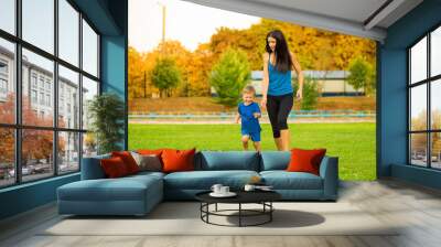 Mother and little son playing ball on grass in summer park Wall mural