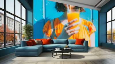 Rear view of beautiful woman is holding orange juice glass at poolside in summer closeup. Wall mural