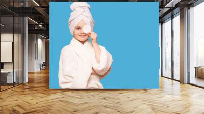 Smiling beautiful kid girl with towel on head hold cotton pad disk cleansing face skin with cleanser. Happy girl remove makeup enjoy healthy clean skincare beauty treatment concept Wall mural