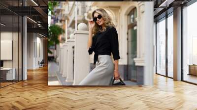 Elegant luxury blond woman with perfect wavy hairs , make up , sunglasses posing outdoor. Casual outfit. Wall mural