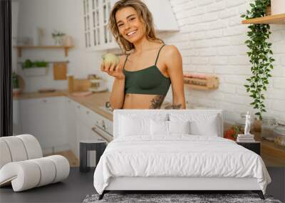 Happy smiling fit woman in activewear looking at camera while standing in the kitchen  after fitness workout at home. Wall mural