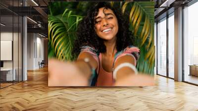 Outdoor  portrait of smiling lovely woman with curly hairs posing over tropical trees and palm leaves. Wall mural