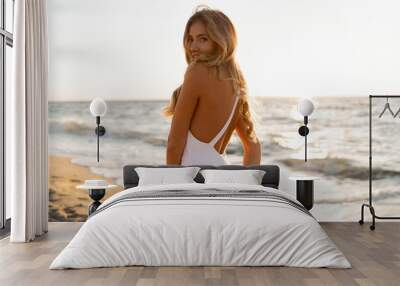 Seductive  blond woman in sexy swimwear posing on the beach in sunset light. Prtfect wavy hairs, tan skim body. Summer tropical mood. Wall mural