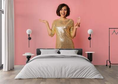 Smiling woman in elergant golden sequin dress holding glass of champagne and  enjoing new year party. Pink background. Wall mural