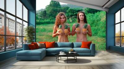 two sexy beautiful sexy girl models in a bikini on the beach and the hands of pineapples cover the chest Wall mural