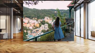 Woman in blue dress enjoying panoramic view of Karlovy Vary, Czech Republic, from a hilltop gazebo, overlooking the famous spa town, historical architecture, and lush green hills in summer Wall mural