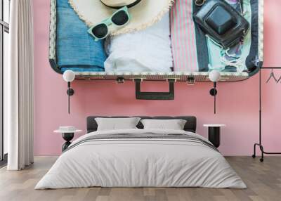 Open suitcase with female clothes for trip on pastel pink. Top view with copy space. Summer concept travel. Wall mural