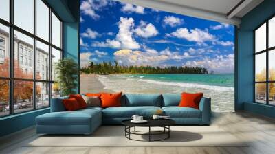 Turquoise water on a tropical sandy beach with a treeline of bahamian pine trees in the background and beautiful clouds in the sky in the Caribbean, Freeport, Bahamas Wall mural