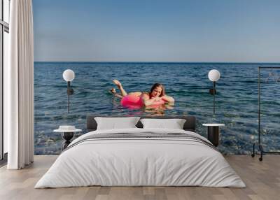 A woman is floating on a pink inflatable raft in the ocean Wall mural