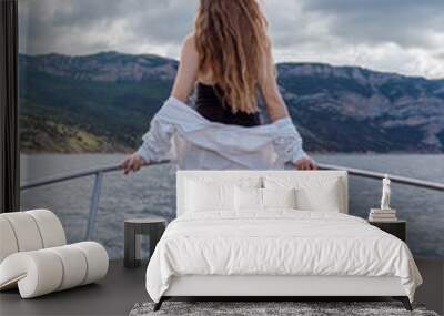 Woman on a yacht. Happy model in a swimsuit posing on a yacht against a blue sky with clouds and mountains Wall mural