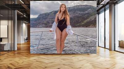 Woman on a yacht. Happy model in a swimsuit posing on a yacht against a blue sky with clouds and mountains Wall mural