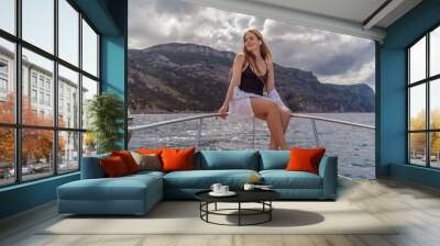 Woman on a yacht. Happy model in a swimsuit posing on a yacht against a blue sky with clouds and mountains Wall mural