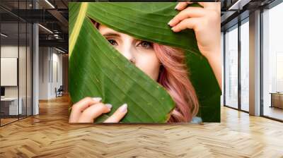 Woman portrait pink hair banana leaf. A beautiful young woman among the huge green leaves of a banana tree. Wall mural