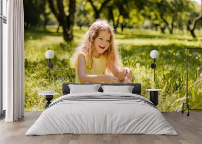 A little girl is sitting with a book in the garden. A girl reads a book on a summer day Wall mural