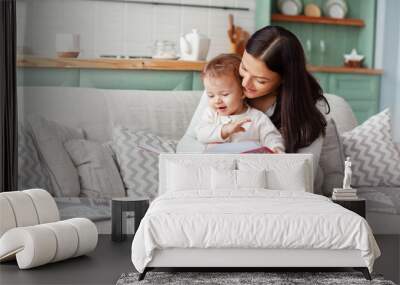 Mom sits on a sofa with a child, reads a book and looks at bright pictures Wall mural