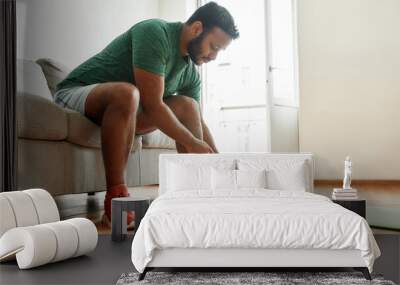 Almost ready. Young active man in sneakers tying shoelaces, preparing for morning workout with dumbbells on a yoga mat at home. Fitness, motivation concept Wall mural