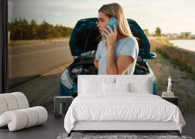 Attractive girl having problems with the car, young woman looking aside and calling for assistance while standing near her broken car with open hood on the road side Wall mural