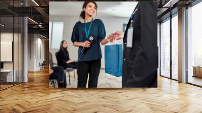 Breaking Down Barriers. Young female speaker receiving gift bag from her male colleague at business meeting, forum. Audience sitting at the conference hall Wall mural