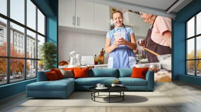 Cheerful teenage girl and lovely grandmother hanging out in kitchen Wall mural