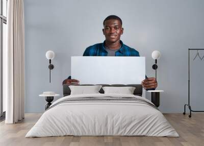 Cheerful young african american man in casual clothes smiling at camera, displaying blank banner ad, holding it in front of him, posing isolated over gray background Wall mural