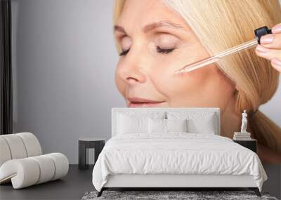 Close-up of a mature lady applies face serum. Wall mural