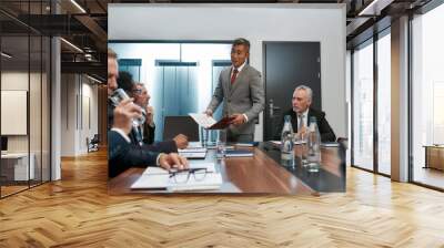 Confident asian businessman in formal wear holding some document and discussing project results with multicultural team while having a meeting in the modern office Wall mural