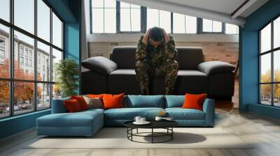 Constant pain. Full length shot of middle aged military man holding his head in pain and depression sitting on the couch. Soldier suffering from psychological trauma. PTSD concept Wall mural