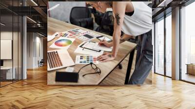 Creative female. Young blonde tattooed female designer making some sketches while standing near office desk. Working with color swatch samples Wall mural