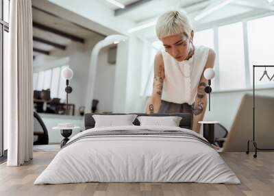 Creative occupation. Young stylish tattooed female designer working on new project while standing near office desk Wall mural