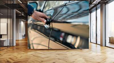 Cropped photo of a male hand opening the door of a black car while standing outdoors Wall mural