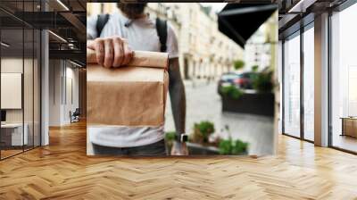 Cropped shot of delivery man holding paper bag while giving away order to a customer. Courier, delivery service concept Wall mural