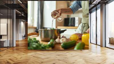 Cropped shot of man, Italian cook pouring a glass of white wine into the pan with chopped vegetables while preparing a meal in the kitchen Wall mural