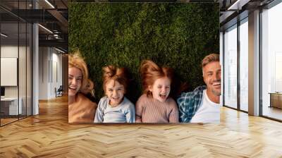 Family vacation. Happy family of four lying on green grass Wall mural