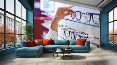 Female hand taking eyeglasses from shelf in optical store Wall mural