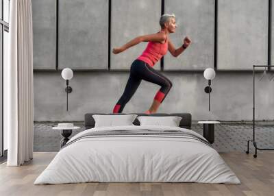 Full of energy. Side view of active middle aged woman in sport clothing jumping while exercising outdoors Wall mural