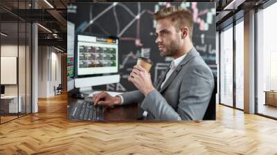 Get your financial power. Portrait of successful trader looking aside and drinking coffee while sitting in front of multiple monitors in the office. Blackboard full of data analyses in background. Wall mural