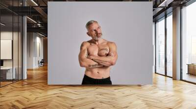 Half naked middle aged muscular man looking aside, showing his body, while posing in studio over grey background Wall mural