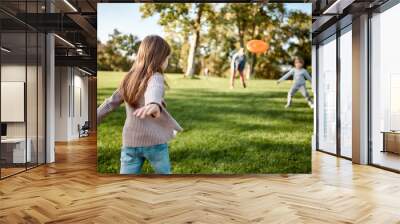 Here we go again. Little girl playing frisbee with her family in the park on a sunny day Wall mural