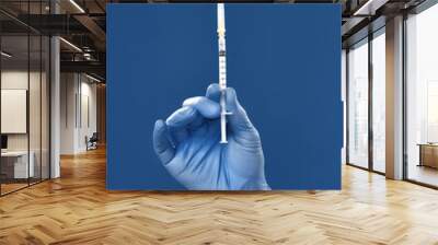 Immunisation. Cropped shot of male doctor hand in blue sterile gloves holding syringe with vaccine from flu, coronavirus, covid-19, isolated against navy blue background Wall mural