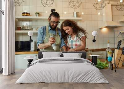 Italian man, chef cook using hand blender while preparing a meal. Young woman, girlfriend in apron pouring olive oil in the pot, helping him in the kitchen Wall mural