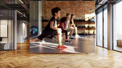 Make your commitment. Portrait of a boy smiling while warming up, exercising together with other kids and female trainer in gym. Sport, healthy lifestyle, physical education concept Wall mural