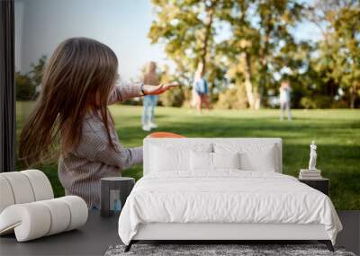 Making memories, breaking the distance. Little girl playing frisbee with her family in the park on a sunny day Wall mural