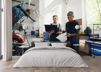 Mechanics holding papers and laptop while examining engine Wall mural