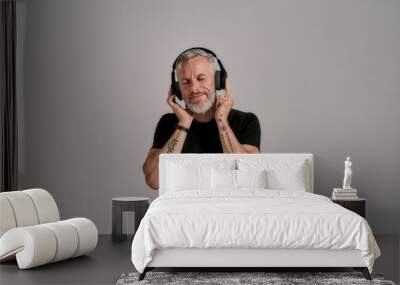 Middle aged muscular man in black t shirt and headphones closing his eyes while listening to music in studio over grey background Wall mural