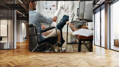 Nice to meet you. Young male office worker in a wheelchair shaking hand to his colleague while working together in the creative office. Disability concept Wall mural