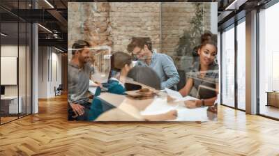 Office life. Multicultural team discussing something and smiling while sitting together behind the glass wall in the modern office Wall mural